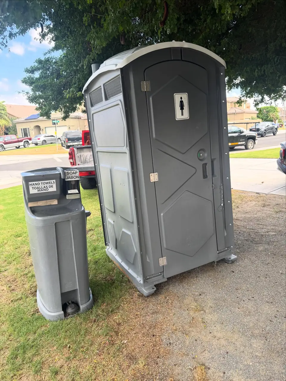 Grey porta potty and a hand-wash station on a grass lawn