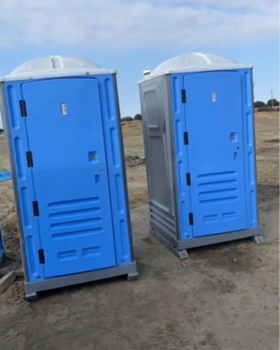 Two standard porta potties on an open dirt lot