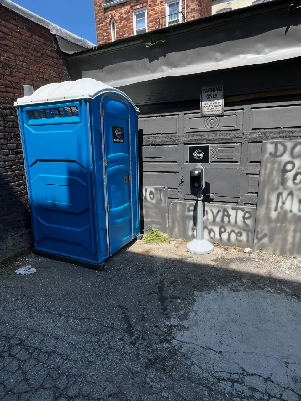 Standard blue porta potty placed beside a garage on a driveway